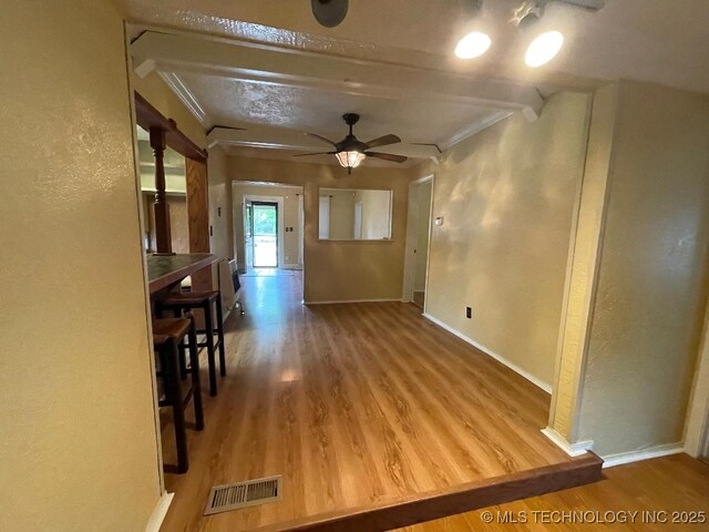 interior space featuring a textured wall, a ceiling fan, baseboards, wood finished floors, and visible vents