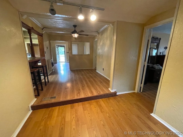 corridor with visible vents, rail lighting, wood finished floors, baseboards, and a textured wall