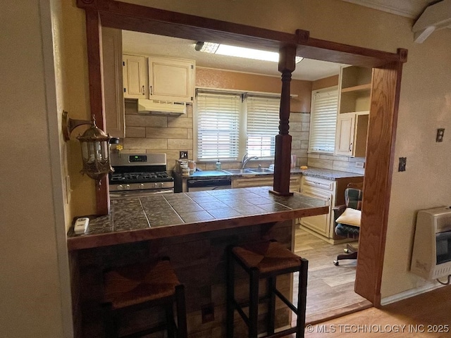 kitchen featuring a sink, stainless steel gas stove, a breakfast bar area, heating unit, and decorative backsplash