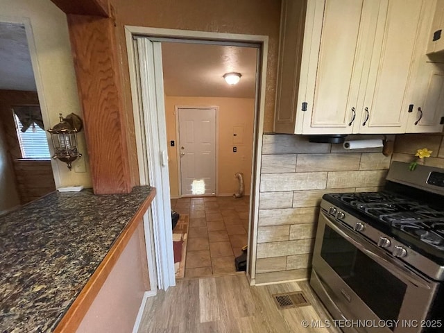 kitchen featuring decorative backsplash, gas range, light wood-type flooring, white cabinets, and dark stone counters