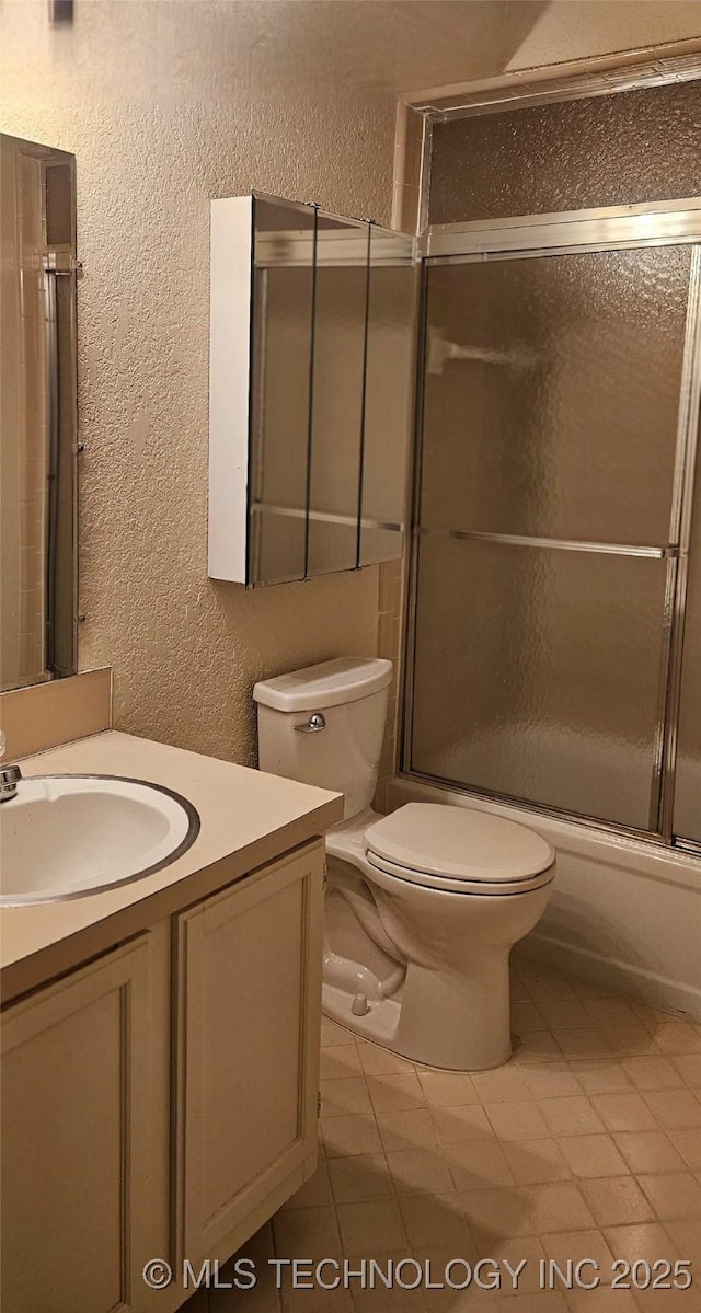 7502 S Winston Pl Unit 203, Tulsa, OK 74136 - full bath featuring a textured wall, vanity, toilet, enclosed tub / shower combo, and tile patterned flooring