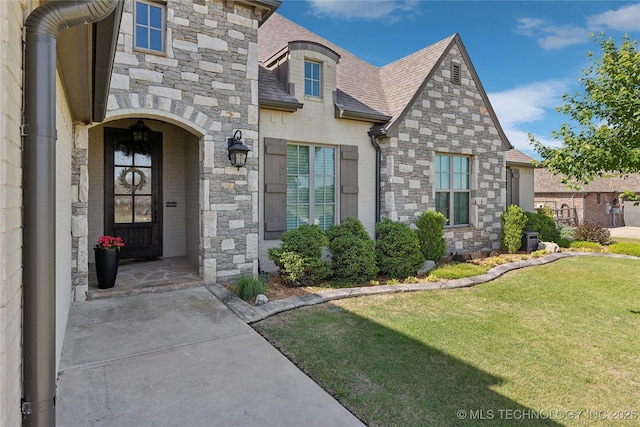19672 E 69th St N, Owasso, OK 74055 - view of exterior entry featuring a shingled roof, stone siding, a lawn, and central AC unit