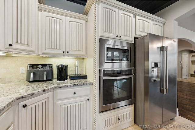 19672 E 69th St N, Owasso, OK 74055 - kitchen with stainless steel appliances, arched walkways, backsplash, and light stone counters