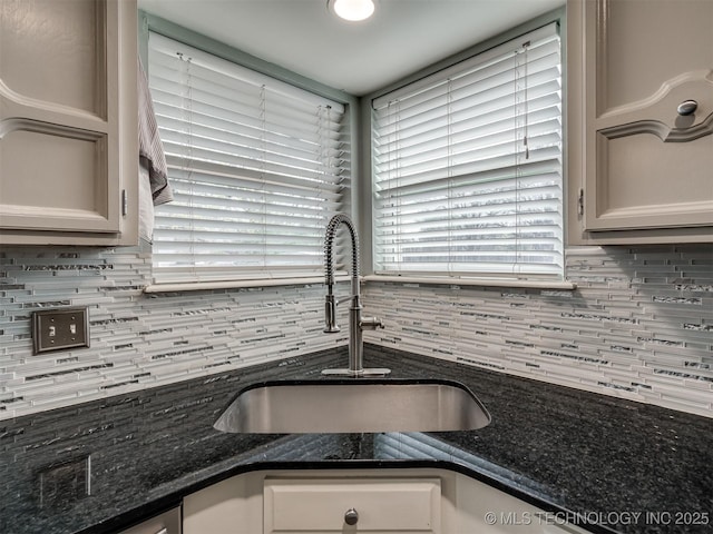 kitchen featuring a sink, dark stone counters, and backsplash