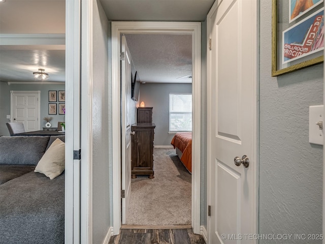 hall with a textured ceiling, baseboards, dark carpet, dark wood-style floors, and a textured wall