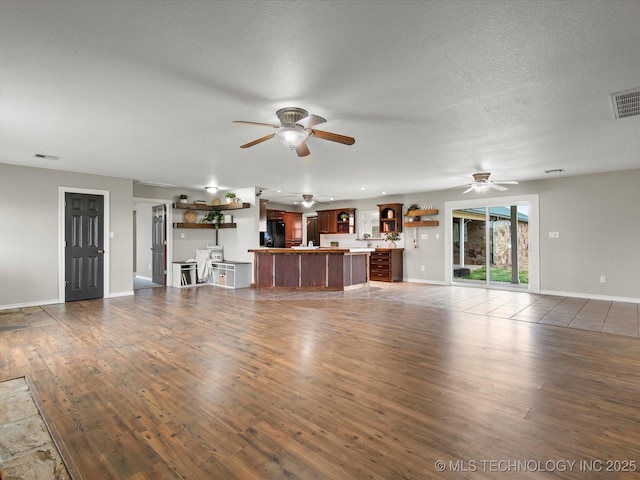 unfurnished living room featuring baseboards, dark wood-style floors, ceiling fan, and visible vents