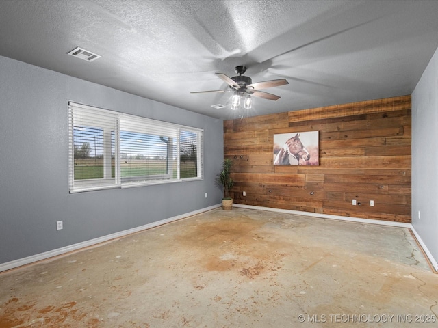 unfurnished room featuring concrete floors, a textured ceiling, wooden walls, ceiling fan, and visible vents