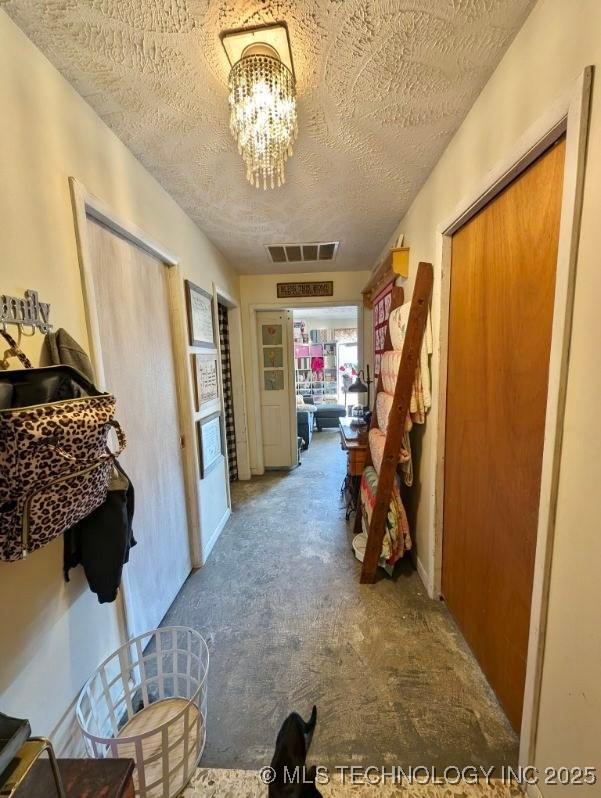 hallway featuring carpet floors, a textured ceiling, visible vents, and an inviting chandelier