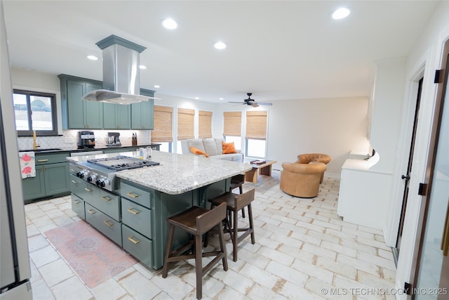 kitchen featuring stainless steel gas cooktop, a kitchen breakfast bar, decorative backsplash, a kitchen island, and ceiling fan