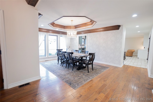 dining room with a raised ceiling, crown molding, wood-type flooring, a chandelier, and baseboards