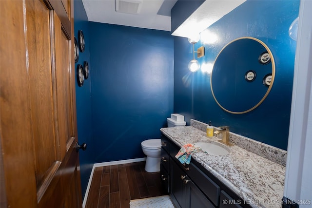half bath featuring toilet, wood finished floors, baseboards, and vanity
