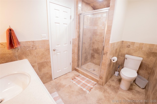 bathroom featuring tile walls, a stall shower, toilet, a wainscoted wall, and tile patterned flooring