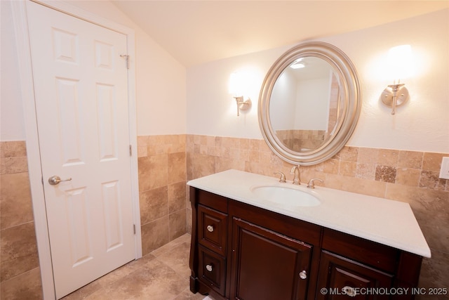 bathroom featuring tile walls, lofted ceiling, vanity, and a wainscoted wall