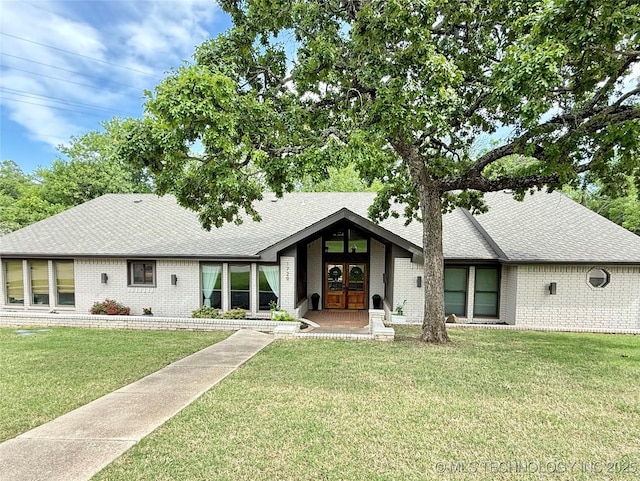 view of front of house featuring brick siding, a front lawn, french doors, and roof with shingles