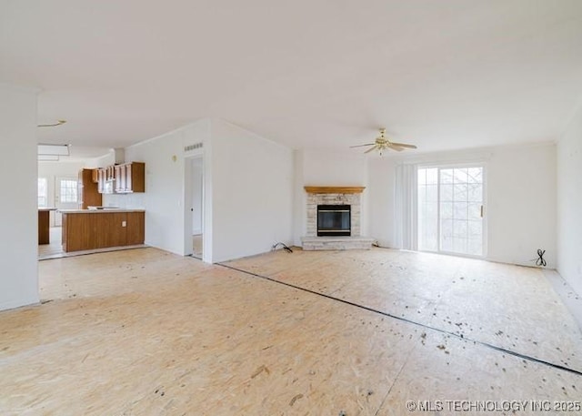 unfurnished living room featuring a ceiling fan and a stone fireplace
