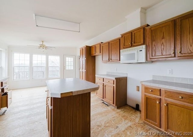 24606 S Red Bud Cir, Afton, OK 74331 - kitchen featuring white microwave, brown cabinets, ceiling fan, and a center island