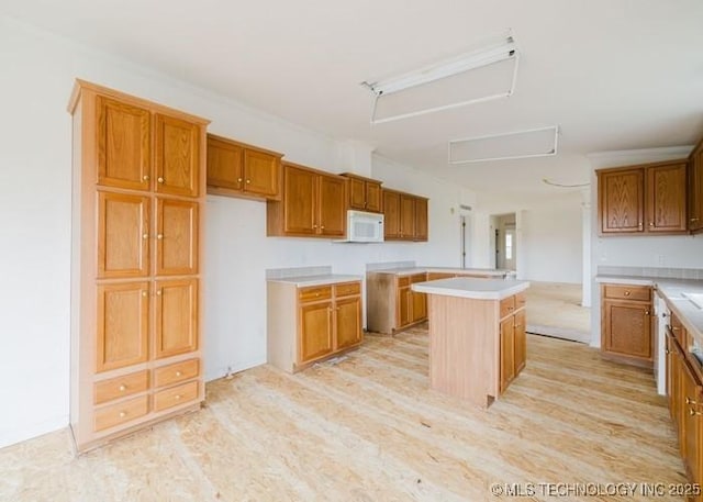 kitchen featuring white microwave, light wood-style flooring, brown cabinetry, and a kitchen island