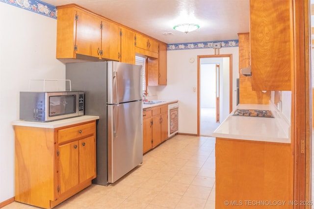 kitchen featuring light countertops, a sink, appliances with stainless steel finishes, and baseboards