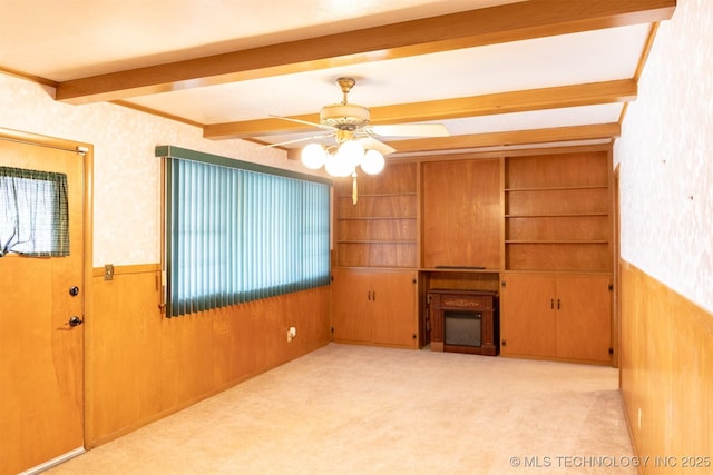 unfurnished living room with a wainscoted wall, ceiling fan, wood walls, and beam ceiling