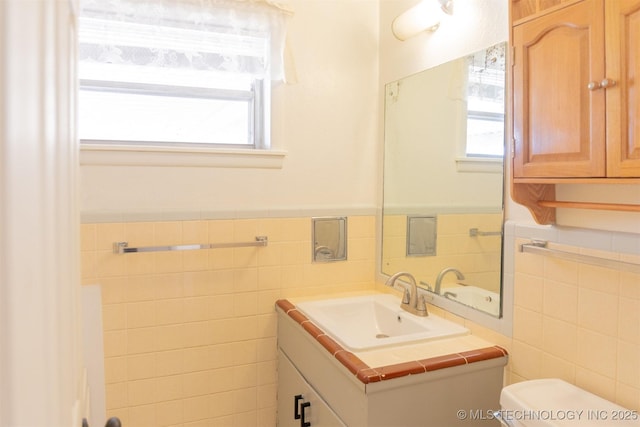 bathroom featuring toilet, vanity, tile walls, and wainscoting