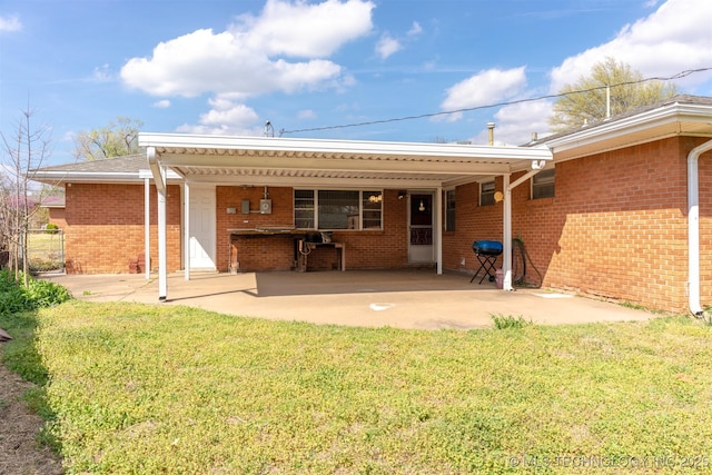 back of house featuring a lawn, an attached carport, a patio, and brick siding
