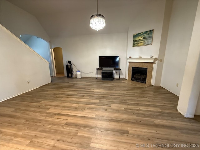 unfurnished living room featuring vaulted ceiling, a chandelier, a fireplace, wood finished floors, and arched walkways