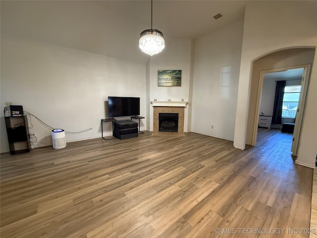 unfurnished living room featuring a notable chandelier, a fireplace, wood finished floors, visible vents, and arched walkways
