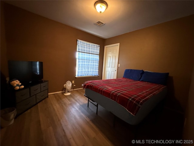 bedroom with baseboards, visible vents, and wood finished floors