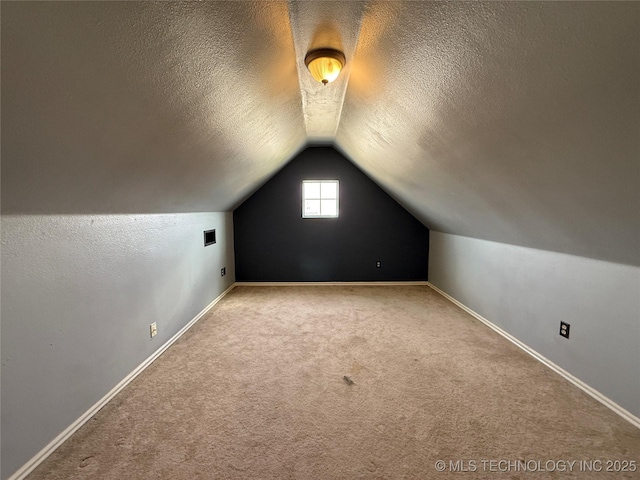 additional living space featuring a textured ceiling, lofted ceiling, carpet flooring, and baseboards