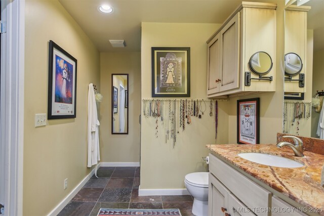 bathroom with vanity, toilet, baseboards, visible vents, and stone tile flooring