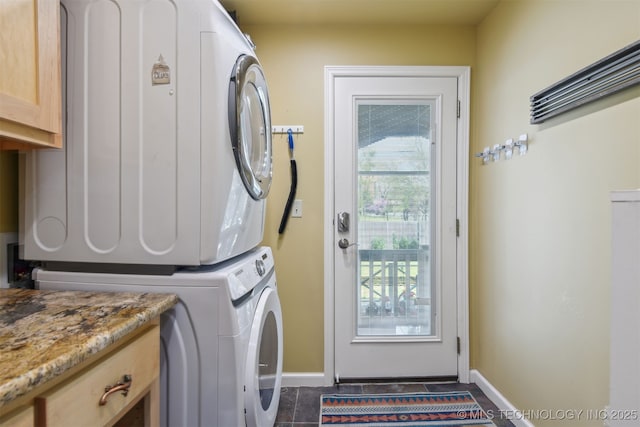 laundry area featuring baseboards, stacked washer and clothes dryer, and cabinet space