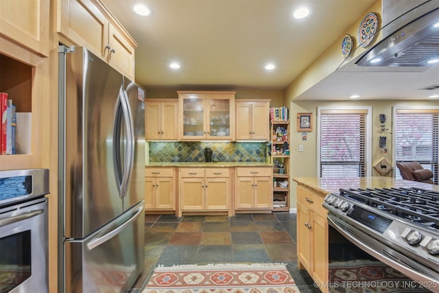 kitchen featuring tasteful backsplash, stainless steel appliances, light brown cabinets, stone finish flooring, and ventilation hood