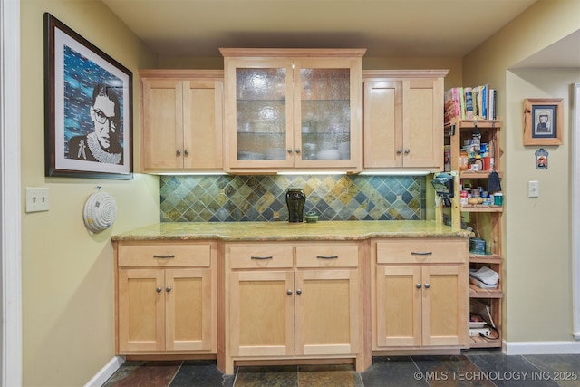 kitchen featuring light brown cabinets, glass insert cabinets, baseboards, and backsplash