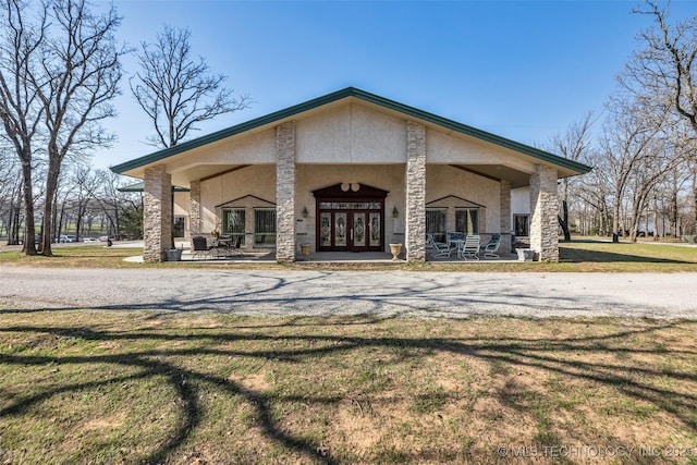exterior space featuring stucco siding, stone siding, a front lawn, and french doors