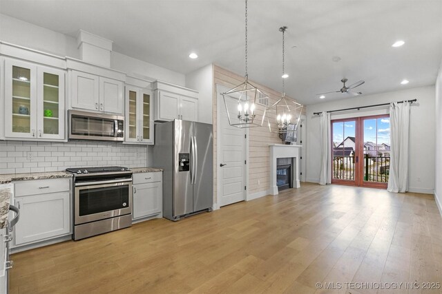 29 Water St Unit 4, Carlton Landing, OK 74432 - kitchen with appliances with stainless steel finishes, backsplash, light stone counters, light wood finished floors, and a glass covered fireplace