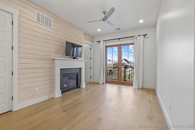 29 Water St Unit 4, Carlton Landing, OK 74432 - unfurnished living room featuring wooden walls, light wood finished floors, ceiling fan, visible vents, and a glass covered fireplace