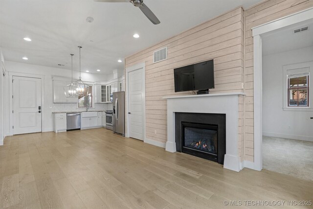 29 Water St Unit 4, Carlton Landing, OK 74432 - unfurnished living room with light wood-style flooring, ceiling fan with notable chandelier, a glass covered fireplace, and visible vents