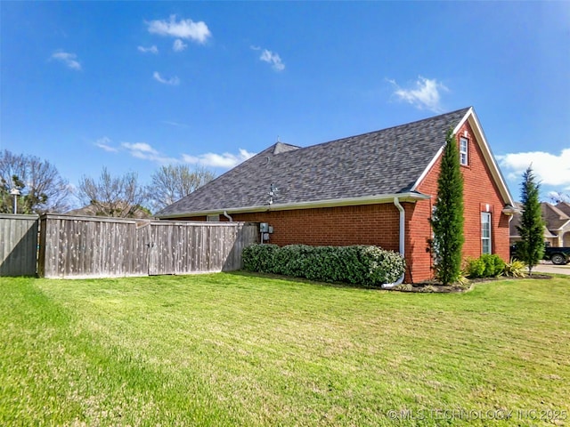 view of side of property featuring roof with shingles, brick siding, fence, and a yard