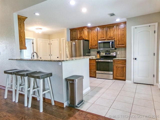 kitchen with light tile patterned floors, stainless steel appliances, a breakfast bar, visible vents, and light stone countertops