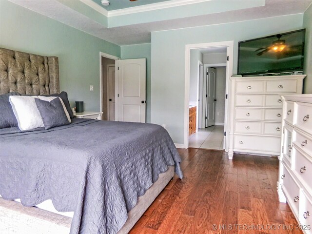 bedroom with a tray ceiling, dark wood-style floors, and baseboards
