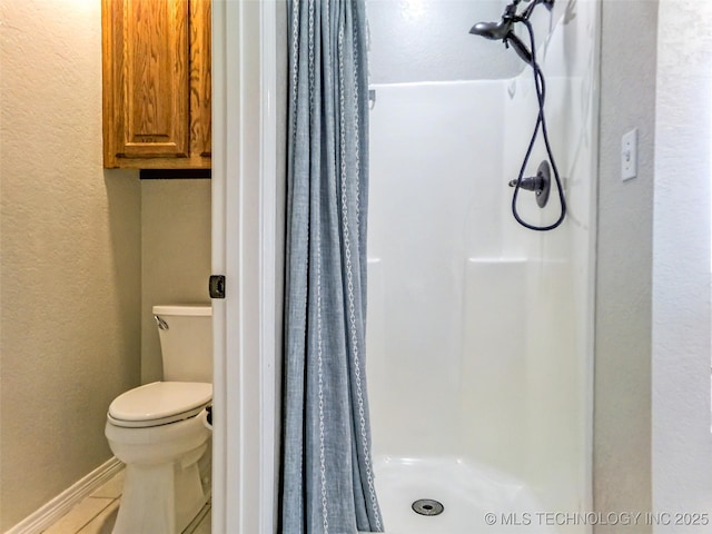 full bath featuring toilet, a textured wall, baseboards, a shower stall, and tile patterned floors