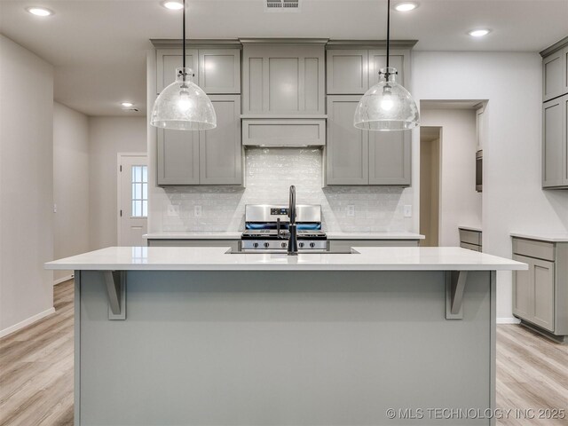 13406 E 124th St, Collinsville, OK 74021 - kitchen with decorative backsplash, light countertops, light wood finished floors, an island with sink, and gray cabinets