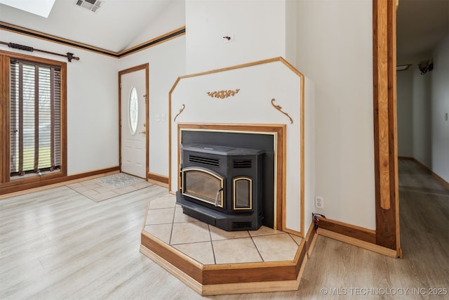 foyer entrance featuring lofted ceiling, a wood stove, baseboards, visible vents, and wood finished floors