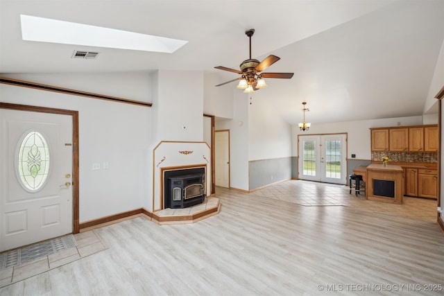 unfurnished living room with light wood-style flooring, visible vents, a skylight, a ceiling fan, and a wood stove