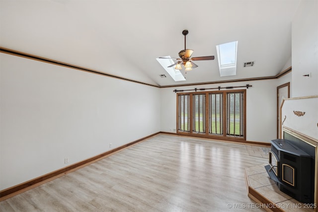 unfurnished living room with visible vents, a wood stove, light wood-type flooring, and vaulted ceiling with skylight