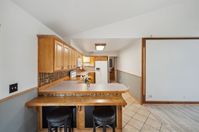 kitchen with decorative backsplash, a peninsula, white appliances, lofted ceiling, and light tile patterned floors