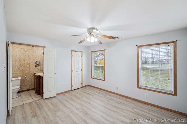 unfurnished bedroom with baseboards, ensuite bath, light wood finished floors, a ceiling fan, and a closet