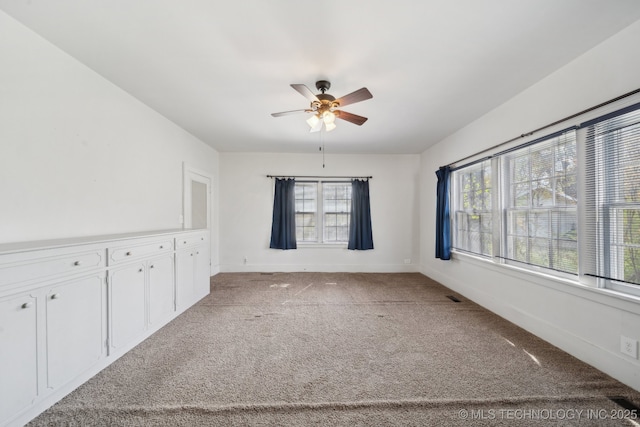 carpeted spare room featuring a wealth of natural light, baseboards, and a ceiling fan