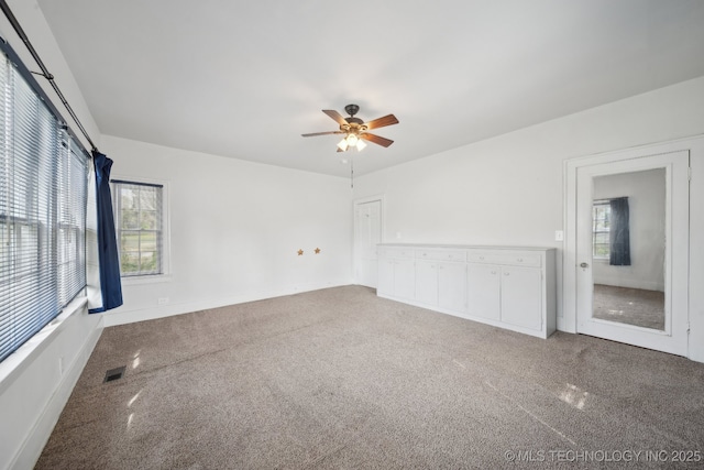 empty room featuring visible vents, carpet floors, and a ceiling fan