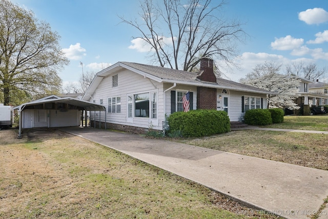 view of side of property featuring driveway, a carport, a chimney, and a yard
